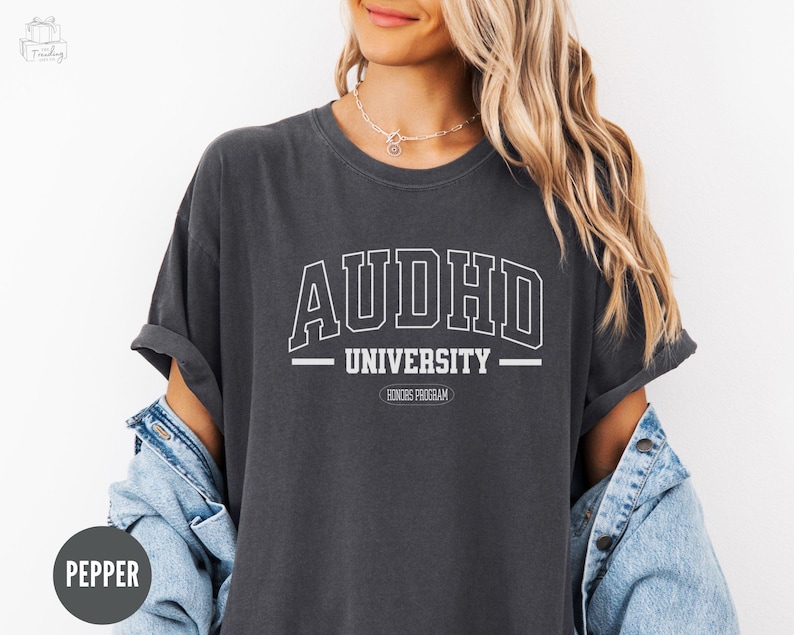 May include: A dark grey t-shirt with the text "AUDHD UNIVERSITY" in white. The text is in a collegiate font style with a banner underneath that reads "HONORS PROGRAM".