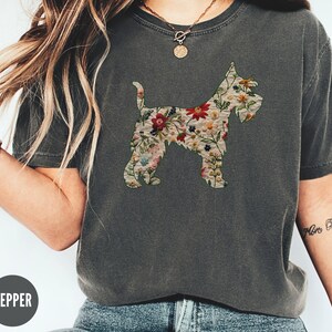 Puede incluir: Una camiseta gris oscuro con un estampado floral de una silueta de perro. El texto "Pepper" es visible en la parte inferior de la imagen.