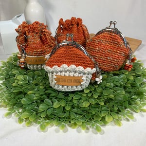 May include: Four crocheted coin purses with orange and white yarn. The purses have a metal clasp and a small leather tag that reads "Hecho con Amor".