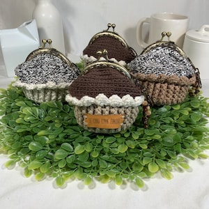May include: Four crocheted coin purses with a brown and white color scheme. The purses have a metal clasp and a brown leather tag that reads "HECHO CON AMOR".