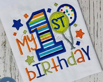 May include: A white onesie with blue, green, and orange embroidery that says "My 1st Birthday". The number one is decorated with stripes and a green and yellow balloon with the word "ST" is in the background.