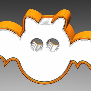 May include: Orange plastic bat-shaped cookie cutter with a white interior. The cutter has a rounded body and two pointed wings.