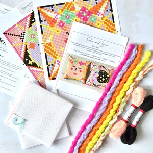 May include: A craft kit with instructions, colorful thread, and canvas. The kit includes a paper chart and needle. The instructions are for a cross-stitch project with a sun and moon design. The finished size is approximately 10cm x 10cm.
