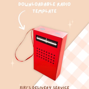May include: A red papercraft radio with a black dial and speaker. The radio has a white strap and says "Kiki's Delivery Service" on the bottom. The image is on a pink and white checkered background.