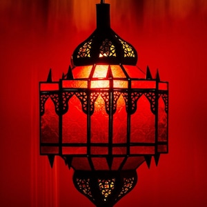 May include: A decorative red lantern with intricate black metalwork and a warm, inviting glow. The lantern features a geometric design with pointed edges and a hanging chain, perfect for adding ambiance to any space.
