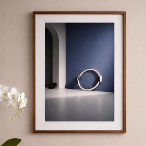 Könnte beinhalten: Gerahmter Druck mit einer minimalistischen Innenszene mit einem Pilates-Ring vor einer blauen Wand. Eine weiße Orchidee in einem Keramiktopf, ein Holztablett mit einer Kerze, einem Seifenspender und gefalteten weißen Handtüchern.