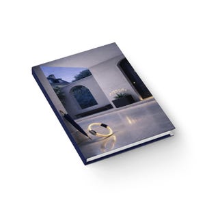 Könnte beinhalten: Ein Hardcover-Buch mit dunkelblauem Einband und einem Foto einer Szene im Freien. Das Bild auf dem Buch zeigt ein modernes architektonisches Design mit einem gewölbten Tor, einer schwarzen Tür und einem dekorativen Ring.