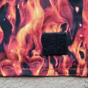 Pode incluir: Um remendo de tecido preto com fecho de velcro, preso a um tecido vermelho e laranja com um padrão de chamas.
