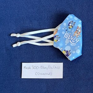 May include: Bluey face mask for children with a blue background and white polka dots. The mask has a white elastic band and features the characters Bluey and Bingo. The text "Bluey" is printed on the mask. The mask is labeled "Mask 300 - Bluey Dia Child (Diamond)".