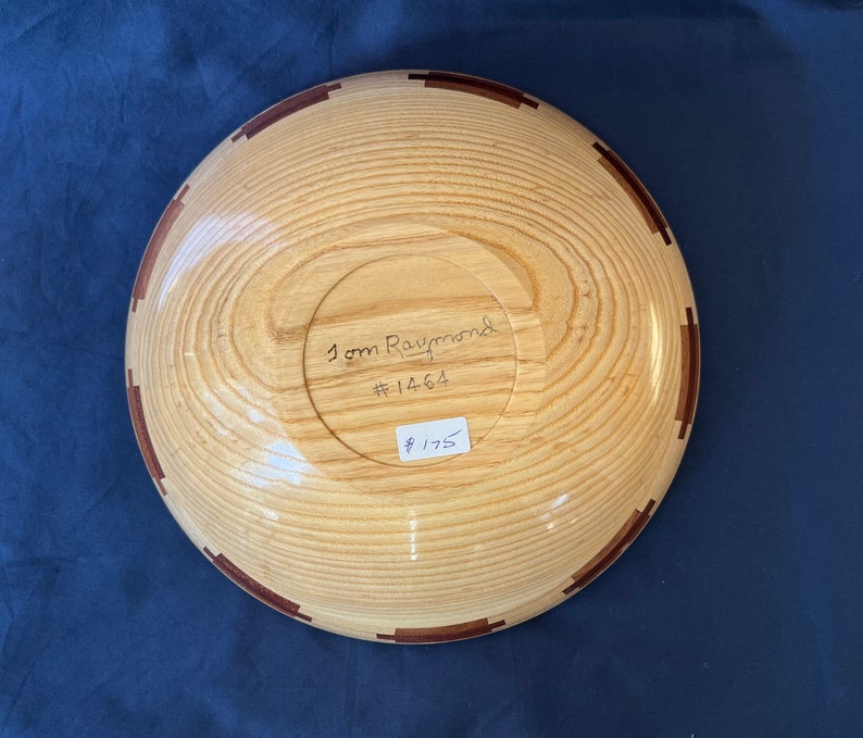K&ouml;nnte beinhalten: Eine Holzschale mit einem braunen und roten Einlegemuster. Die Schale ist signiert mit "Tom Raymond #1464" und kostet 175 &euro;.