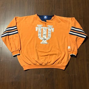 May include: Orange sweatshirt featuring a silver and white "IU" logo. Sleeves have three white and navy blue stripes. Navy blue collar and cuffs. The Starter logo is on the sleeve. A vintage sports item.