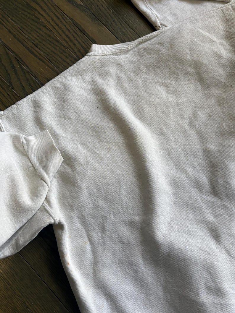 Może przedstawiać: Jasnoszara bluza z okrągłym dekoltem i długimi rękawami. Tkanina ma lekko teksturowany wygląd. Odzież wykonana jest z miękkiego materiału, odpowiedniego do noszenia na co dzień.