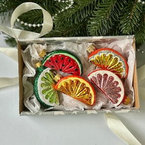 May include: A set of six glass Christmas ornaments shaped like fruit slices. The ornaments are in a white box with tissue paper. The ornaments are red, orange, yellow, green, and pink.