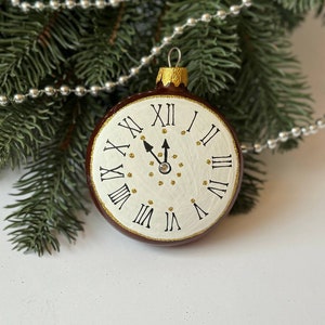 May include: A brown and white Christmas bauble shaped like a clock face with Roman numerals. The clock face has gold accents and a black hand pointing to the twelve.