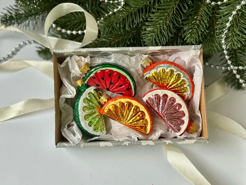 May include: A set of six glass Christmas ornaments shaped like fruit slices. The ornaments are in a white box with tissue paper. The ornaments are red, orange, yellow, green, and pink.