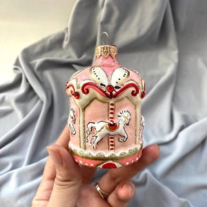 Pu&ograve; includere: Ornamento natalizio a forma di giostra rosa con cavalli bianchi e dettagli dorati. L'ornamento presenta un design decorativo con dettagli rossi e bianchi. Una decorazione festiva per le vacanze.