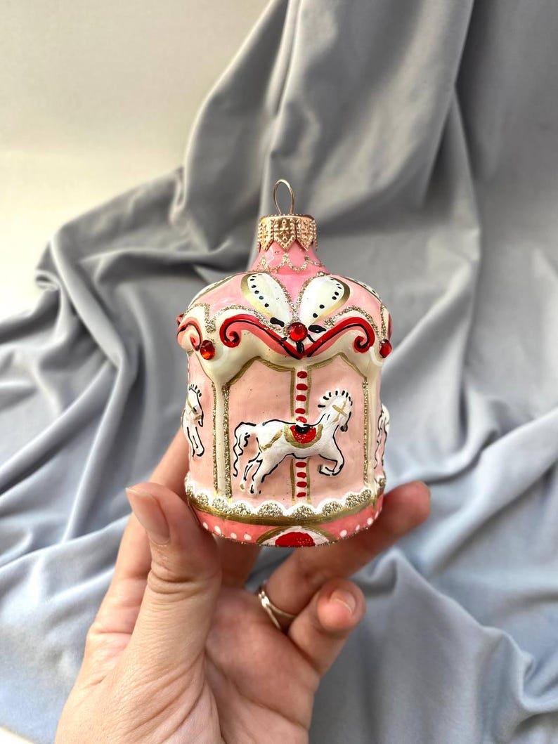 Pu&ograve; includere: Ornamento natalizio a forma di giostra rosa con cavalli bianchi e dettagli dorati. L'ornamento presenta un design decorativo con dettagli rossi e bianchi. Una decorazione festiva per le vacanze.