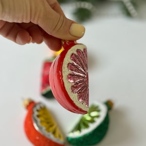 May include: Four glass ornaments shaped like fruit slices. The ornaments are red, green, and yellow. The ornaments are decorated with glitter.