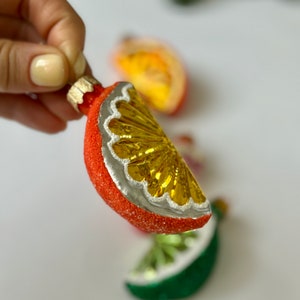 May include: A red and yellow glass ornament shaped like a slice of orange. The ornament has a silver rim and a textured surface.