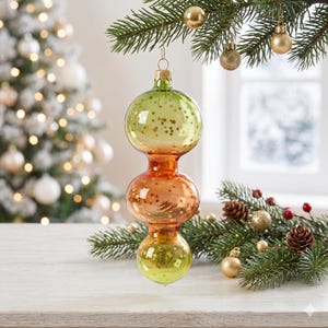May include: A vertical glass Christmas ornament featuring three stacked, rounded bulbous sections. The top and bottom sections are light green, while the middle section is orange. All sections are decorated with small, gold-colored star shapes.