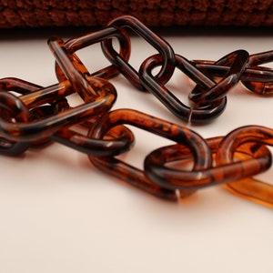 May include: A close-up of a brown plastic chain. The chain is made of oval links and has a tortoiseshell pattern.