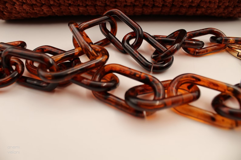 May include: A close-up of a brown plastic chain. The chain is made of oval links and has a tortoiseshell pattern.