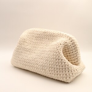 Pu&ograve; includere: Una borsa a uncinetto color crema con una forma unica e curva. La borsa &egrave; realizzata con un filato spesso e testurizzato e ha un aspetto morbido e naturale.