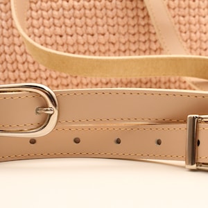 Puede incluir: Dos correas de cuero beige con hebillas plateadas. Las correas est&aacute;n cosidas y tienen un brillo sutil.