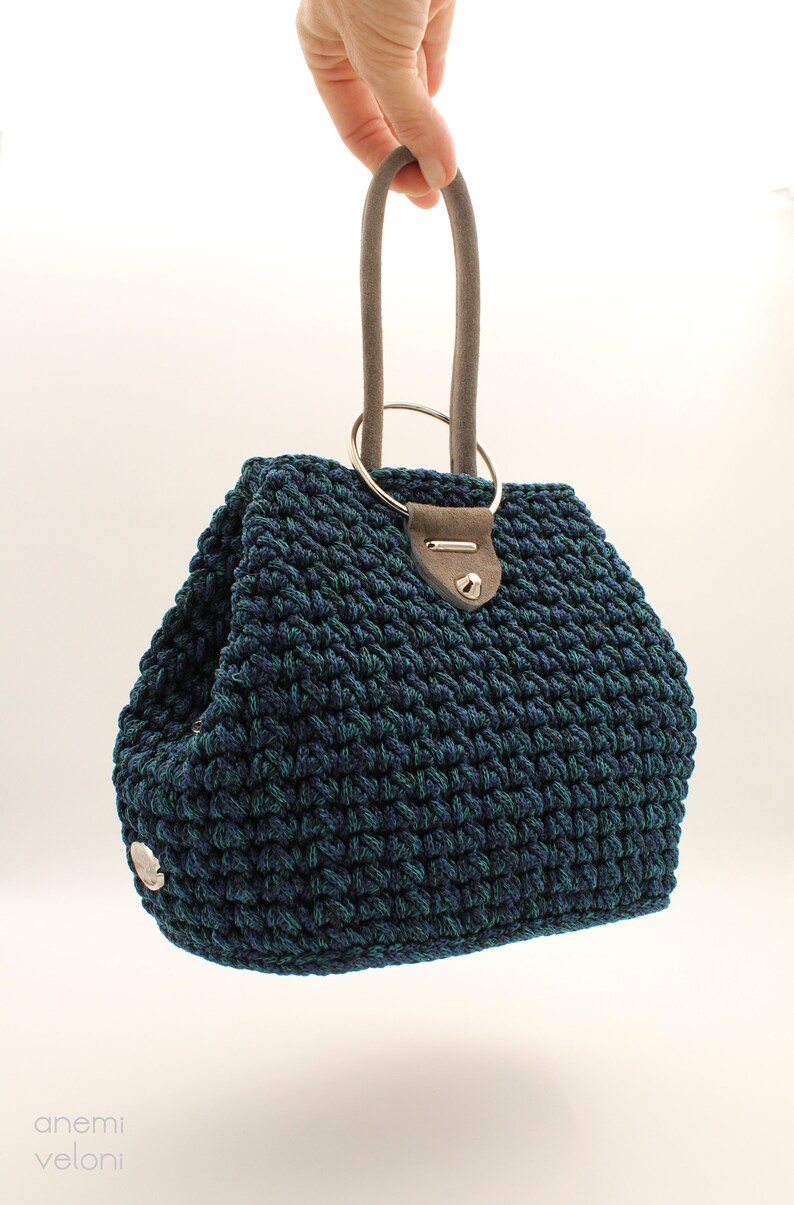 May include: A dark blue and green crocheted handbag with a silver ring handle and a gray suede strap.