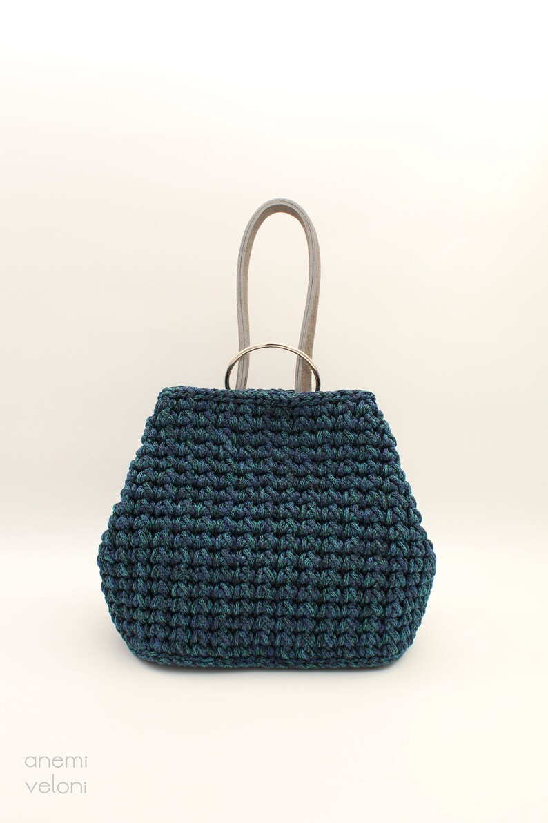 May include: A dark blue and green crocheted tote bag with a silver ring handle and light gray leather straps.