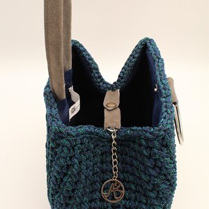 May include: A blue and green crocheted handbag with a suede handle and a silver chain with a metal charm that says "AB".