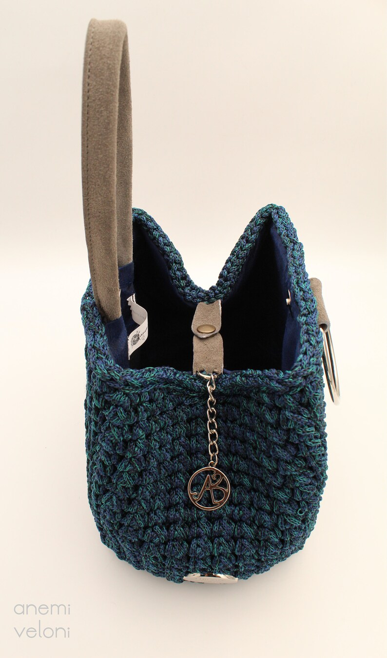May include: A blue and green crocheted handbag with a suede handle and a silver chain with a metal charm that says "AB".
