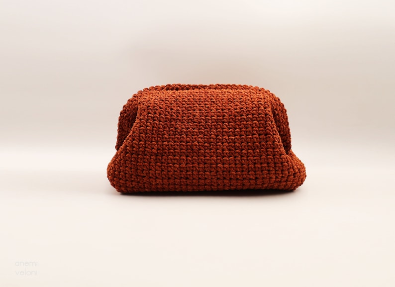 May include: A rust-coloured crocheted pouch or bag. The pouch is made of a thick, textured yarn and has a rounded, slightly puffy shape.