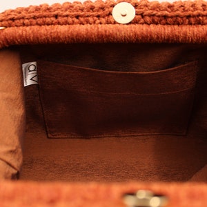 May include: The inside of a brown crocheted bag with a brown fabric lining and a small pocket. The bag has a gold metal clasp and a label that says "a/v handmade bags".
