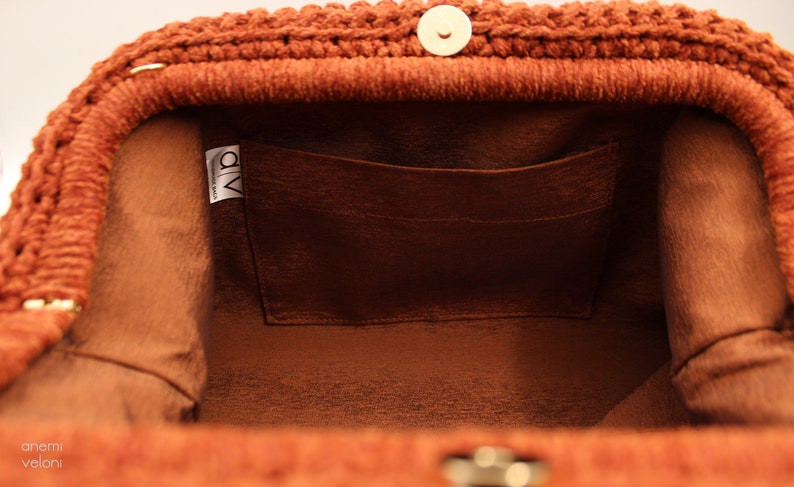 May include: The inside of a brown crocheted bag with a brown fabric lining and a small pocket. The bag has a gold metal clasp and a label that says "a/v handmade bags".