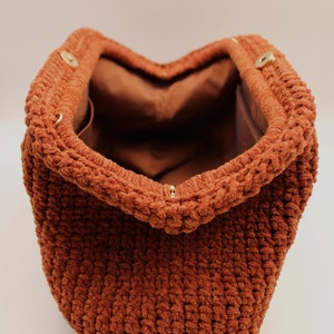 May include: A brown crocheted bag with a soft, fuzzy texture. The bag is open and the inside is lined with brown fabric.