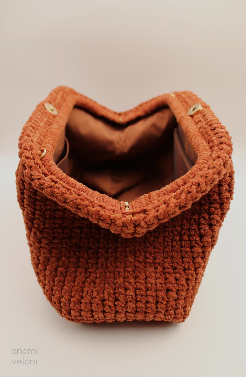 May include: A brown crocheted bag with a soft, fuzzy texture. The bag is open and the inside is lined with brown fabric.