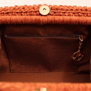 May include: The inside of a brown crocheted handbag with a zipped pocket and a gold-coloured key chain.