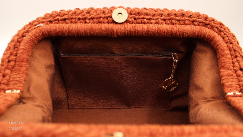 May include: The inside of a brown crocheted handbag with a zipped pocket and a gold-coloured key chain.