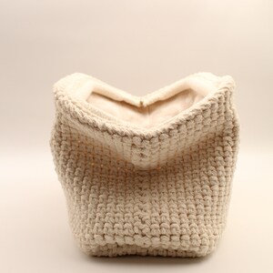 Pu&ograve; includere: Un cesto di stoccaggio in crochet color crema con una superficie morbida e testurizzata. Il cesto &egrave; vuoto e aperto, rivelando l'interno.