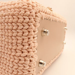 Puede incluir: Un bolso tote de crochet rosa claro con fondo de cuero y pies de metal plateado. El bolso est&aacute; hecho con un hilo grueso y texturizado.