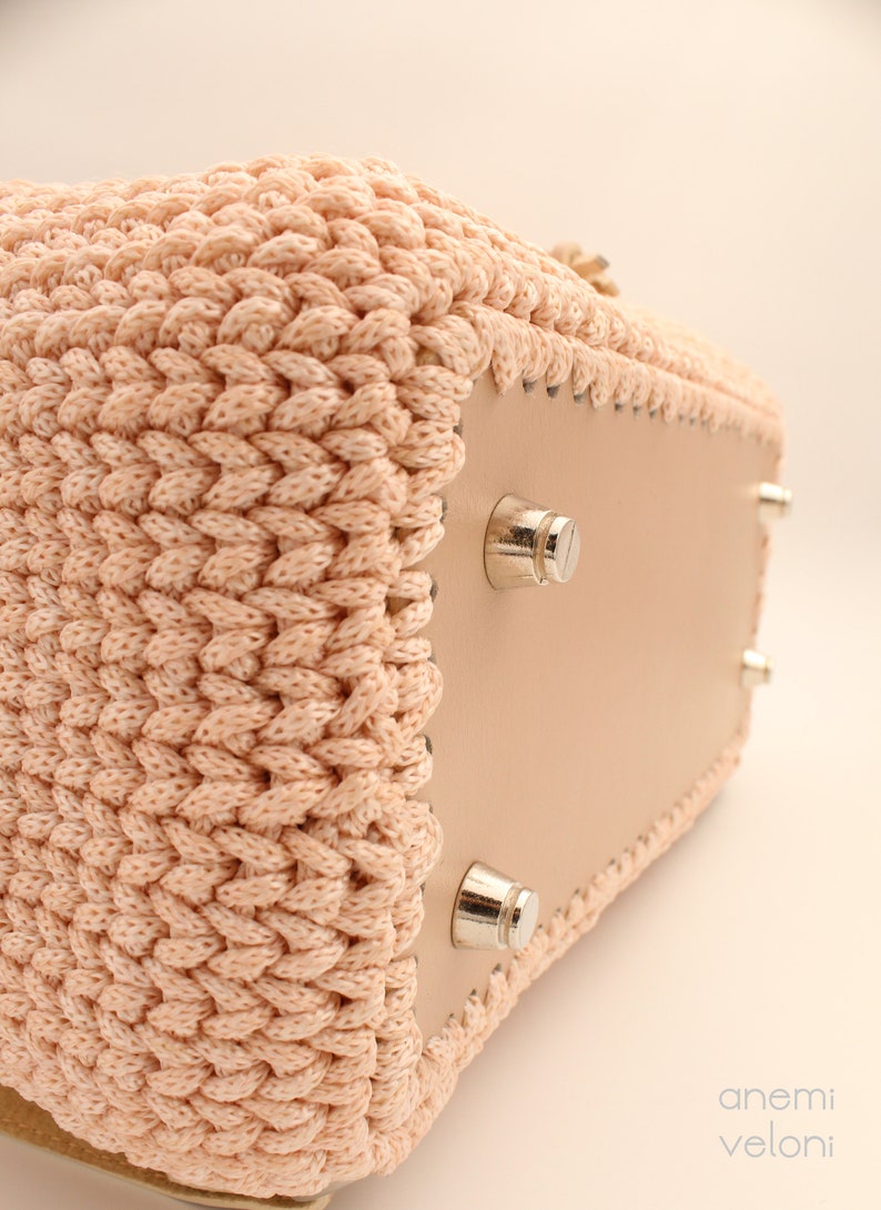 Puede incluir: Un bolso tote de crochet rosa claro con fondo de cuero y pies de metal plateado. El bolso est&aacute; hecho con un hilo grueso y texturizado.
