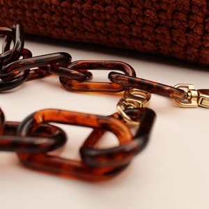 May include: A brown tortoiseshell chain with a gold clasp. The chain is made of large, rectangular links.