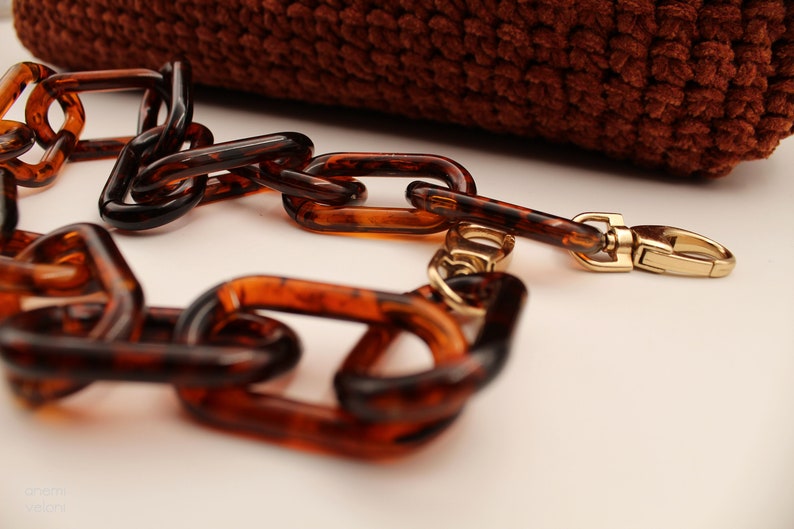 May include: A brown tortoiseshell chain with a gold clasp. The chain is made of large, rectangular links.