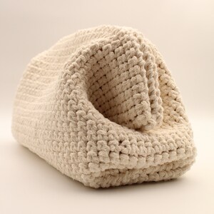 Pu&ograve; includere: Una borsa in crochet color crema realizzata con corda di cotone spessa. La borsa &egrave; piegata su se stessa, mostrando la trama del tessuto a uncinetto.