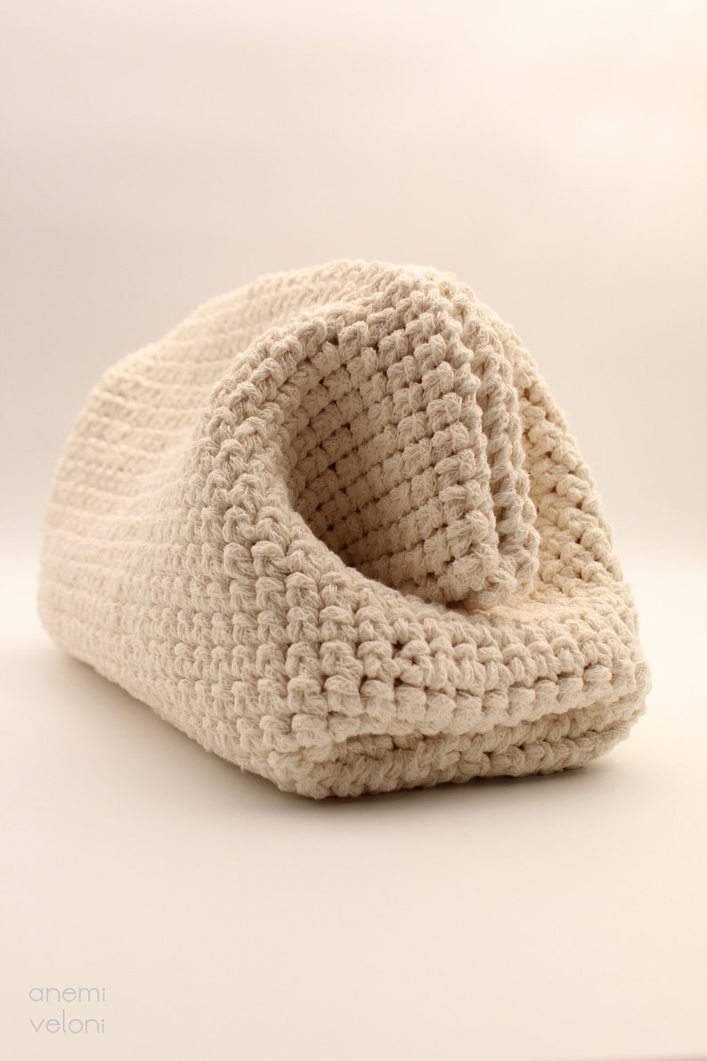 Pu&ograve; includere: Una borsa in crochet color crema realizzata con corda di cotone spessa. La borsa &egrave; piegata su se stessa, mostrando la trama del tessuto a uncinetto.