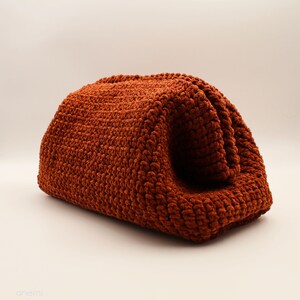 May include: A rust-coloured crocheted bag with a soft, fuzzy texture. The bag is folded in half and has a rounded shape.