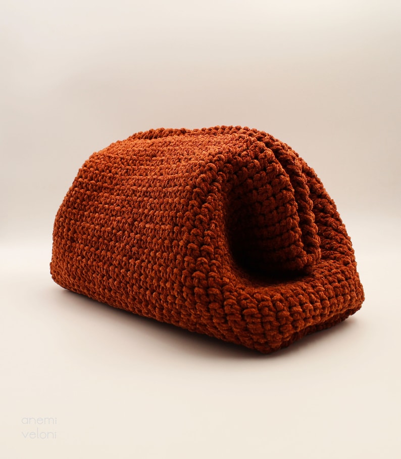 May include: A rust-coloured crocheted bag with a soft, fuzzy texture. The bag is folded in half and has a rounded shape.