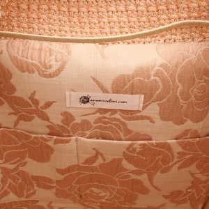 Puede incluir: El interior de una bolsa de mano de crochet de color melocot&oacute;n con un forro de estampado floral. El forro es de color beige claro con un estampado floral de color melocot&oacute;n. Una etiqueta blanca con el texto "anemivefoni.com" est&aacute; cosida en el forro.