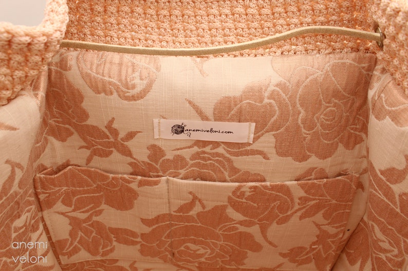 Puede incluir: El interior de una bolsa de mano de crochet de color melocot&oacute;n con un forro de estampado floral. El forro es de color beige claro con un estampado floral de color melocot&oacute;n. Una etiqueta blanca con el texto "anemivefoni.com" est&aacute; cosida en el forro.